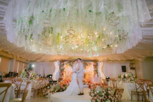 Bride and groom standing on an elegantly decorated wedding stage with floral and chandelier lighting.